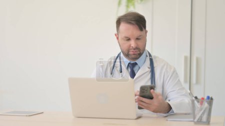 Téléchargez les photos : Jeune médecin travaillant sur ordinateur portable et Smartphone - en image libre de droit