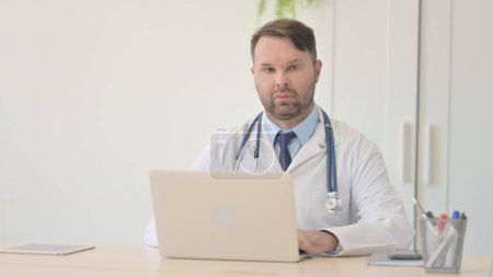 Téléchargez les photos : Jeune médecin travaillant sur ordinateur portable regardant vers la caméra - en image libre de droit