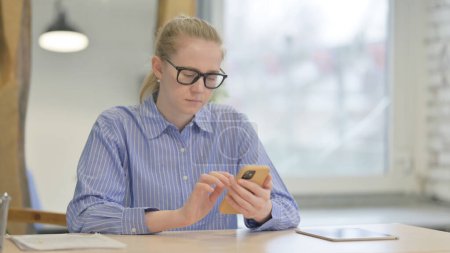 Téléchargez les photos : Jeune femme utilisant un téléphone intelligent au travail - en image libre de droit