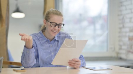 Téléchargez les photos : Jeune femme célébrant tout en lisant le rapport d'affaires au travail - en image libre de droit