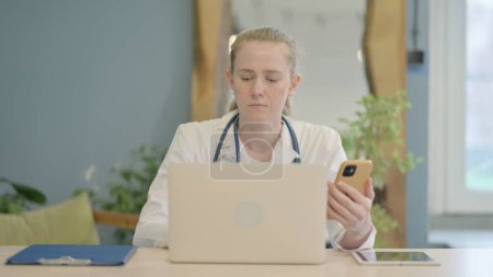Téléchargez les photos : Médecin féminin travaillant sur ordinateur portable et Smartphone en clinique - en image libre de droit