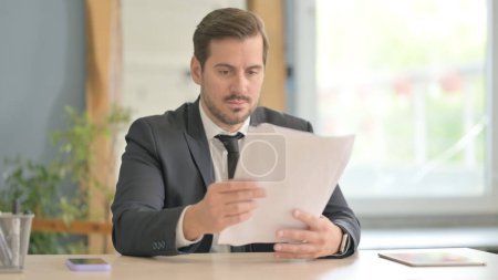 Téléchargez les photos : Homme d'affaires lisant des documents au travail, paperasserie - en image libre de droit