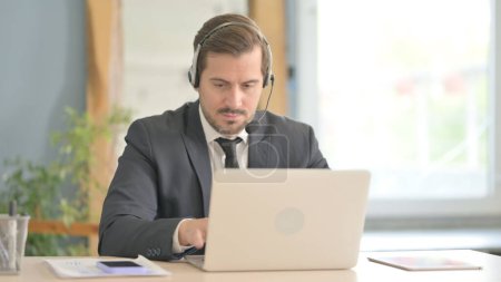 Téléchargez les photos : Homme d'affaires avec casque de travail sur ordinateur portable - en image libre de droit
