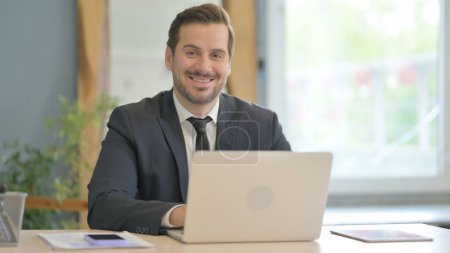 Photo for Businessman Smiling at Camera while Working on Laptop - Royalty Free Image