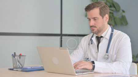 Téléchargez les photos : Médecin masculin travaillant sur ordinateur portable en clinique - en image libre de droit
