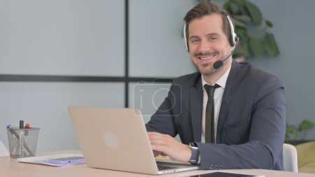 Foto de Empresario con auriculares sonriendo a cámara en call center - Imagen libre de derechos