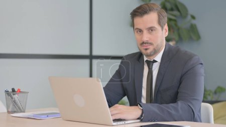Photo for Businessman Working on Laptop Looking toward Camera - Royalty Free Image