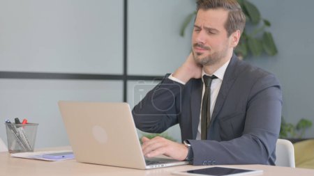 Téléchargez les photos : Homme d'affaires avec douleur au cou travaillant sur ordinateur portable - en image libre de droit
