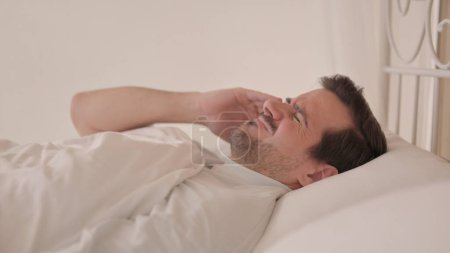 Téléchargez les photos : Vue latérale du jeune homme avec maux de tête au lit - en image libre de droit