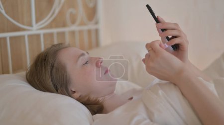 Foto de Vista lateral de la mujer joven usando Smartphone en la cama - Imagen libre de derechos
