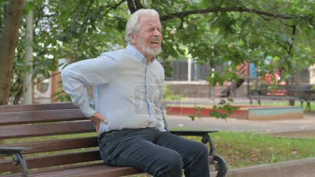 Foto de Anciano mayor sentado al aire libre con dolor de espalda - Imagen libre de derechos