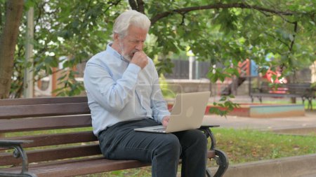 Téléchargez les photos : Toux senior vieil homme en utilisant ordinateur portable en plein air - en image libre de droit