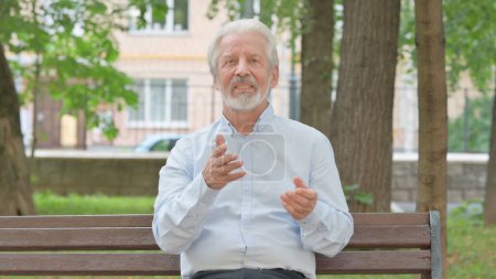 Téléchargez les photos : Parler vieil homme âgé bloguant tout en étant assis dans le parc - en image libre de droit