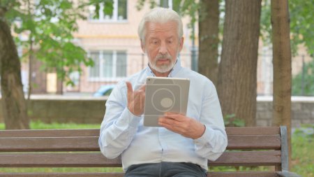 Photo for Senior Old Man Doing Video Chat on Tablet while Sitting in Park - Royalty Free Image