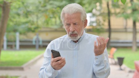 Téléchargez les photos : Vieil homme âgé bouleversé se faire choquer sur Smartphone extérieur - en image libre de droit