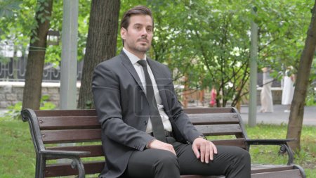 Téléchargez les photos : Sérieux jeune homme d'affaires assis en plein air - en image libre de droit