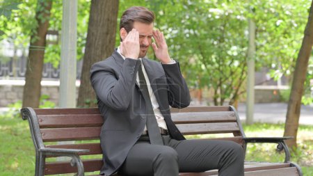 Téléchargez les photos : Fatigué jeune homme d'affaires assis en plein air avec mal de tête - en image libre de droit