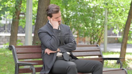 Téléchargez les photos : Jeune homme d'affaires endormi assis à l'extérieur sur le banc - en image libre de droit