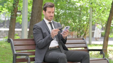 Téléchargez les photos : Jeune homme d'affaires faisant des achats en ligne sur le téléphone tout en étant assis à l'extérieur - en image libre de droit