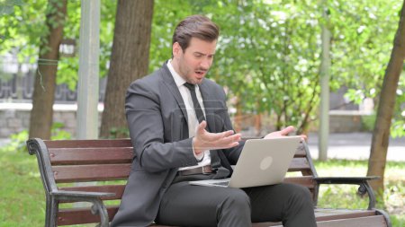 Téléchargez les photos : Jeune homme d'affaires choqué par la perte sur ordinateur portable en plein air - en image libre de droit