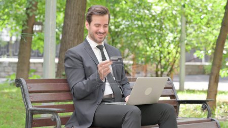 Téléchargez les photos : Jeune homme d'affaires excité pour le succès des achats en ligne sur ordinateur portable en plein air - en image libre de droit