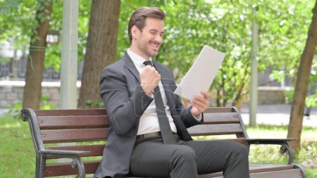 Téléchargez les photos : Jeune homme d'affaires Célébration en lisant des documents en plein air - en image libre de droit