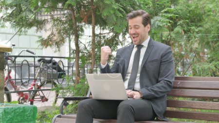 Foto de Emocionado hombre de negocios de mediana edad celebrando el éxito en el ordenador portátil al aire libre - Imagen libre de derechos