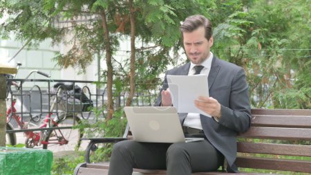 Téléchargez les photos : Moyen Age Homme d'affaires se sentant bouleversé tout en lisant contrat et en utilisant ordinateur portable en plein air - en image libre de droit