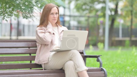 Téléchargez les photos : Vieille femme âgée avec douleur au cou travaillant sur ordinateur portable en plein air - en image libre de droit