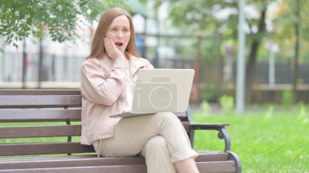 Téléchargez les photos : Vieille femme âgée avec mal de dents travaillant sur ordinateur portable en plein air - en image libre de droit