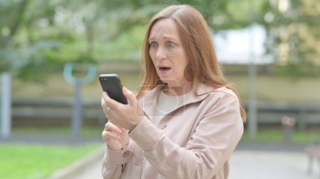 Téléchargez les photos : Bouleversé senior vieille femme obtenez choqué sur Smartphone en plein air - en image libre de droit