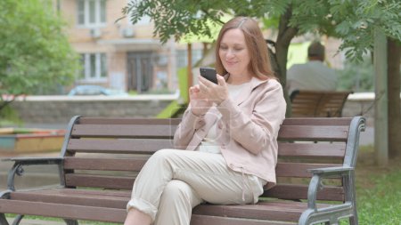 Photo for Modern Old Woman using Smartphone while Sitting on Bench - Royalty Free Image