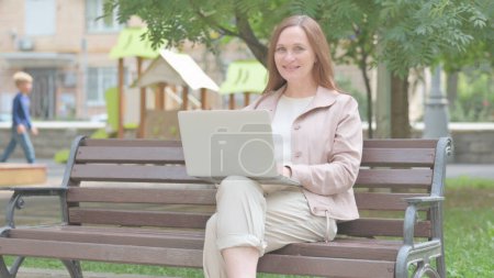 Photo for Modern Old Woman Smiling at Camera while Working on Laptop Outdoor - Royalty Free Image
