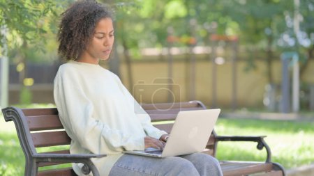 Téléchargez les photos : Jeune femme africaine travaillant sur ordinateur portable en plein air - en image libre de droit