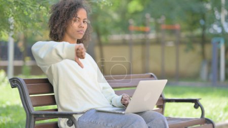 Téléchargez les photos : Pouces vers le bas par jeune femme africaine sur ordinateur portable en plein air - en image libre de droit