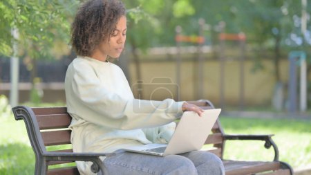 Téléchargez les photos : Jeune femme africaine quittant le banc extérieur après avoir travaillé sur ordinateur portable - en image libre de droit