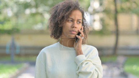 Téléchargez les photos : Jeune femme africaine parlant au téléphone en plein air - en image libre de droit