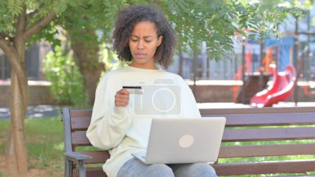 Téléchargez les photos : Femme africaine occasionnelle bouleversé par l'échec de paiement en ligne sur ordinateur portable en plein air - en image libre de droit