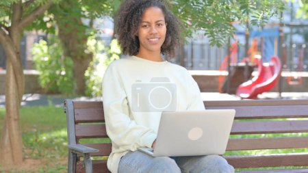 Photo for Casual African Woman Smiling at Camera while Working on Laptop Outdoor - Royalty Free Image
