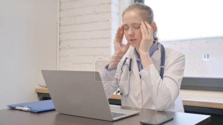 Foto de Médico femenino con dolor de cabeza mientras trabaja en el ordenador portátil - Imagen libre de derechos