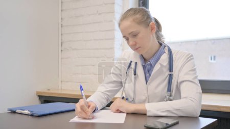 Téléchargez les photos : Médecin Féminin rédigeant un rapport médical, faisant de la paperasserie à l'hôpital - en image libre de droit