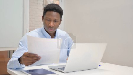 Téléchargez les photos : Homme d'affaires africain lisant des documents au travail - en image libre de droit