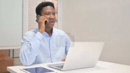 Téléchargez les photos : Un homme d'affaires africain parle au téléphone au travail - en image libre de droit