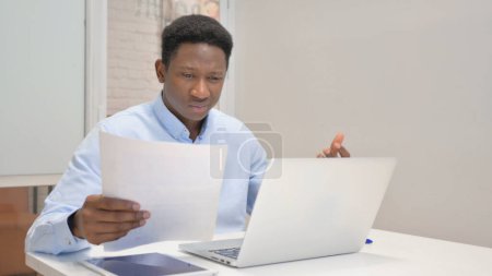 Photo for African Businessman Feeling Upset while Reading Contract and Using Laptop - Royalty Free Image