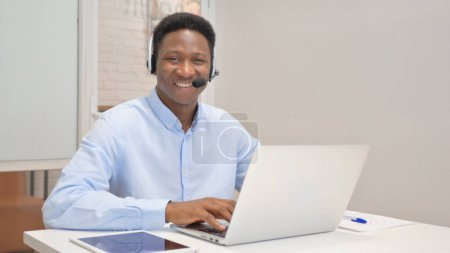 Téléchargez les photos : Homme africain souriant avec casque regardant la caméra dans le centre d'appels - en image libre de droit