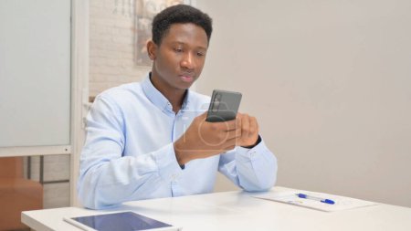 Téléchargez les photos : Africain Homme d'affaires Naviguer sur Internet sur le téléphone au bureau - en image libre de droit
