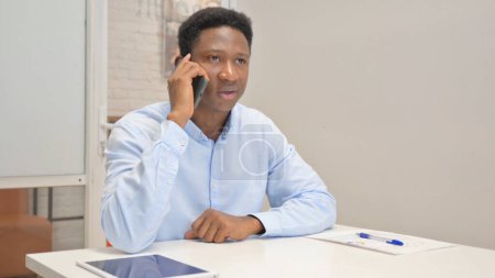Téléchargez les photos : Un homme d'affaires africain parle au téléphone au bureau - en image libre de droit