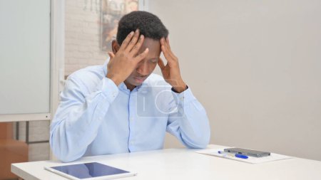 Foto de Empresario africano con dolor de cabeza mientras está sentado en la oficina - Imagen libre de derechos