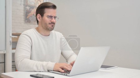 Foto de Negar el rechazo del hombre de mediana edad mientras usa el ordenador portátil en la oficina - Imagen libre de derechos
