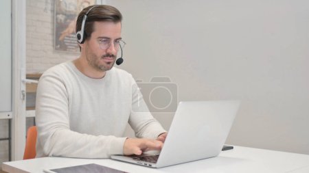 Photo for Young Man with Headset Working on Laptop in Call Center - Royalty Free Image